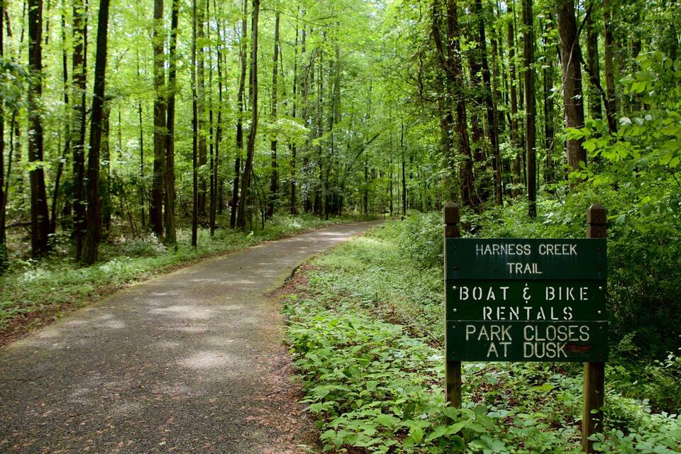 Trilha na floresta com uma placa indicando aluguel de barcos e bicicletas, e fechamento do parque ao anoitecer.