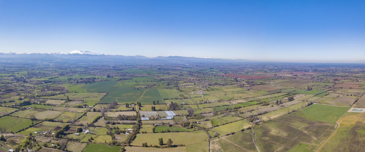 A vast agricultural landscape with fields, small houses, and distant mountains.