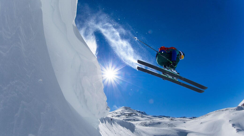 A skier in mid-air performing a jump over a snow-covered slope with the sun shining brightly in the background.