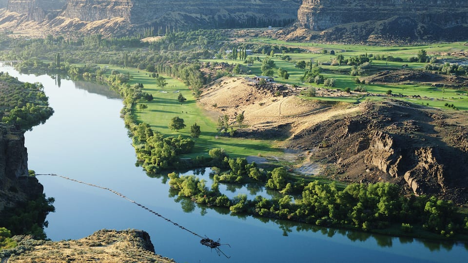 A river winding through a valley with a helicopter flying over.