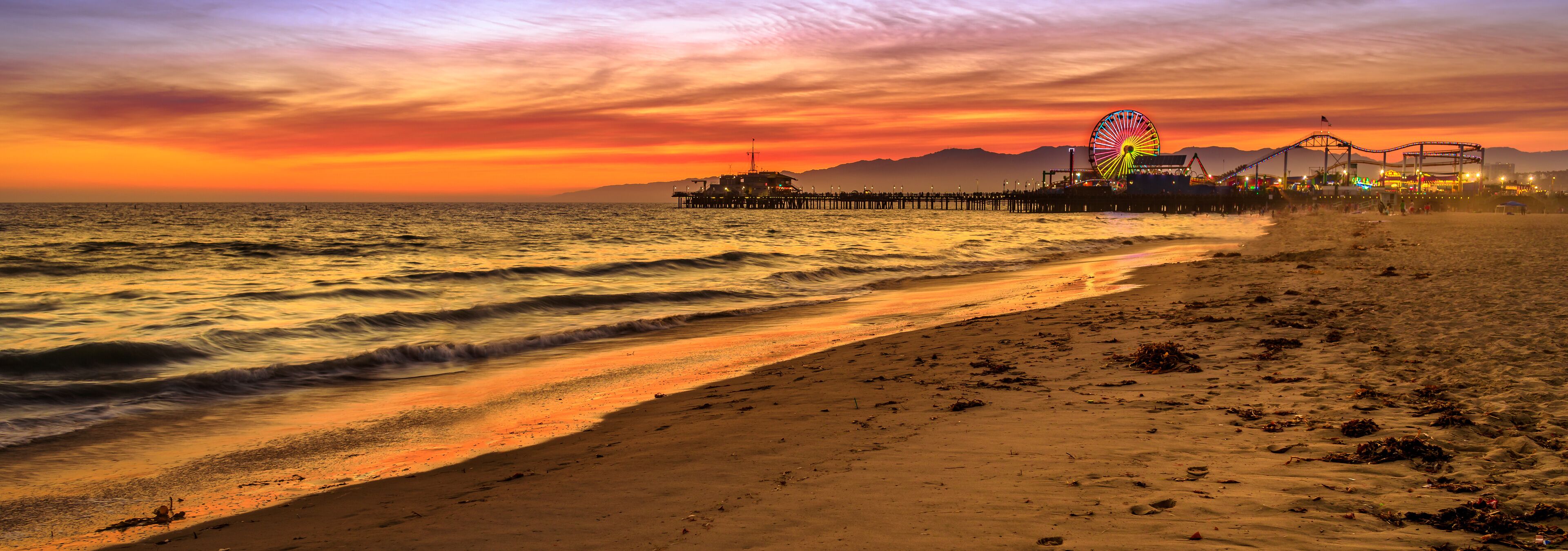 Santa Monica Historic Landmark, California, United States. Amazing landscape of iconic Santa Monica Pier at orange red sunset sky from beach on Paficif Ocean. Banner panorama background.