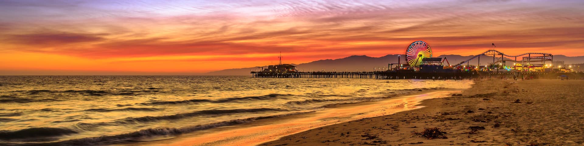 Santa Monica Historic Landmark, California, United States. Amazing landscape of iconic Santa Monica Pier at orange red sunset sky from beach on Paficif Ocean. Banner panorama background.