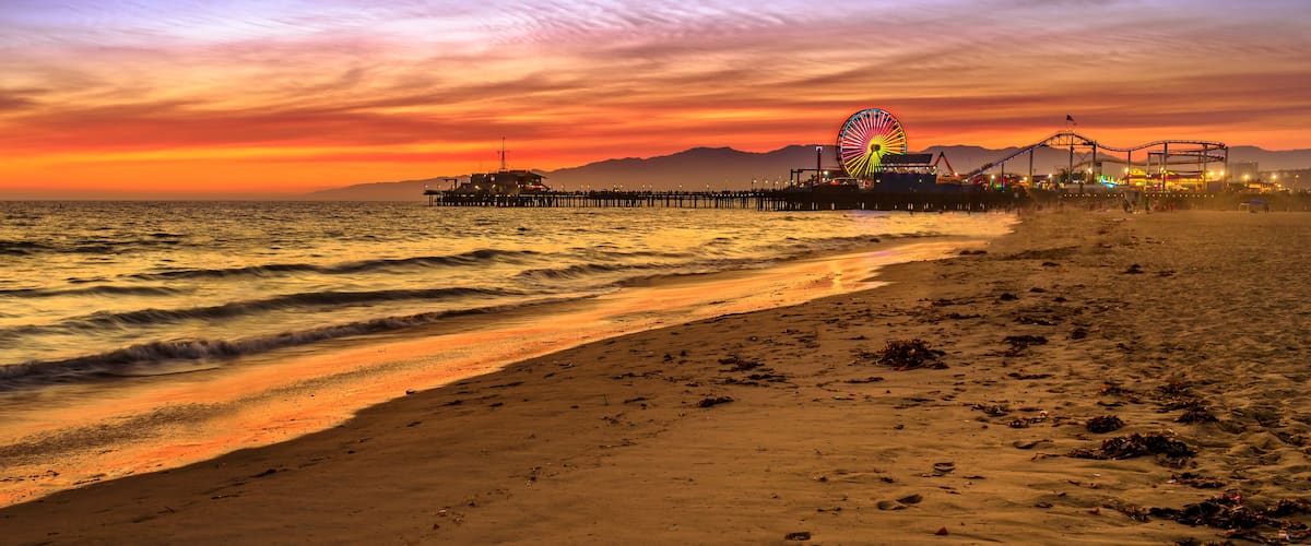 A beach at sunset with a pier and amusement park in the background.