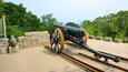 A historical cannon with a wooden carriage, positioned on a concrete platform with stone walls and greenery in the background.