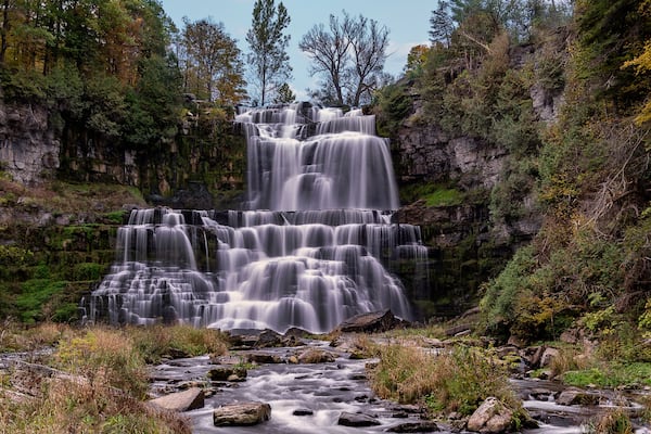 Une cascade Ă plusieurs niveaux, entourĂ©e dâune forĂȘt dense et de falaises rocheuses.