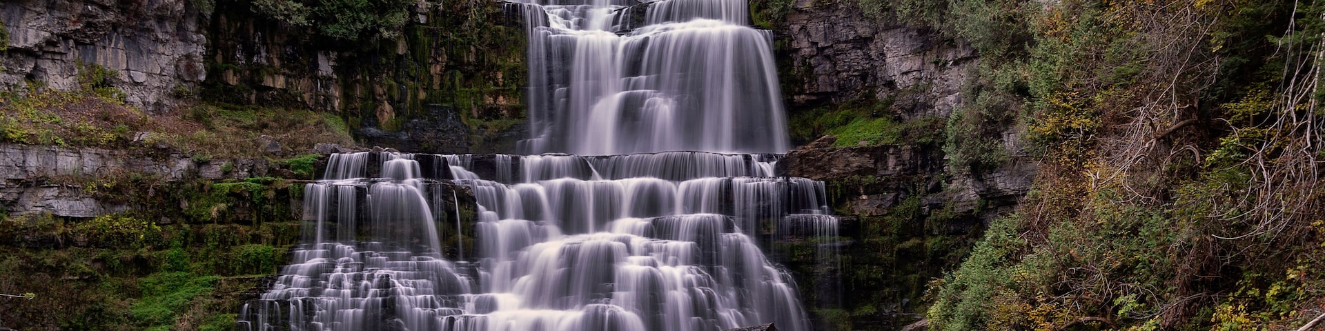 Une cascade Ă plusieurs niveaux, entourĂ©e dâune forĂȘt dense et de falaises rocheuses.