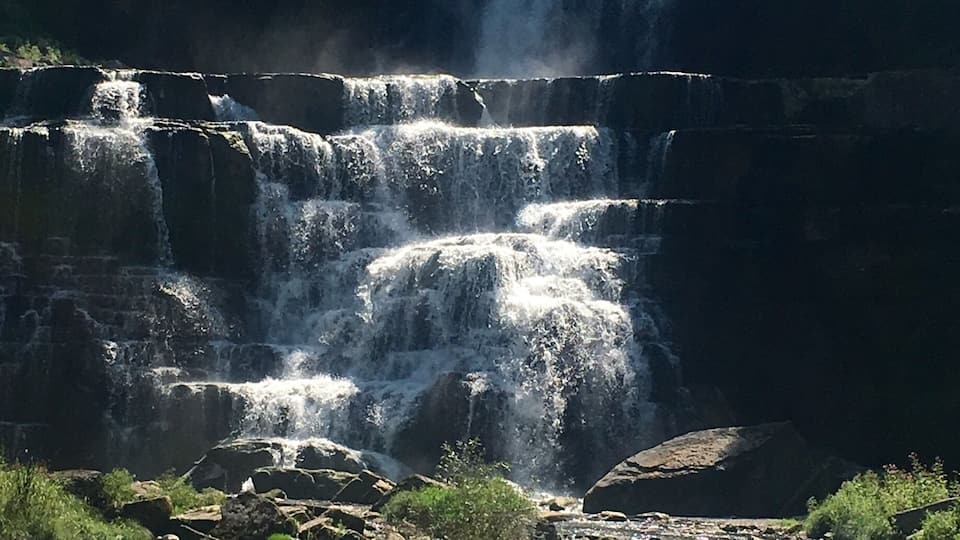 A multi-tiered waterfall surrounded by rocks and greenery.