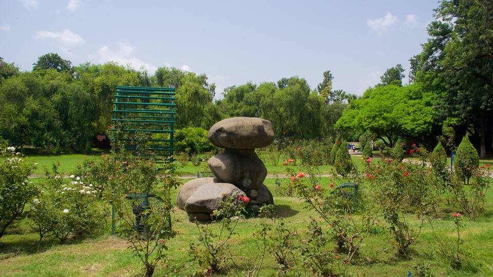 A stone sculpture of stacked rocks in a park with green grass, flowering bushes, and trees.