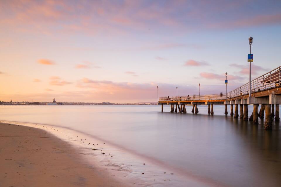 Un muelle se adentra en aguas tranquilas al atardecer, bajo un cielo despejado.