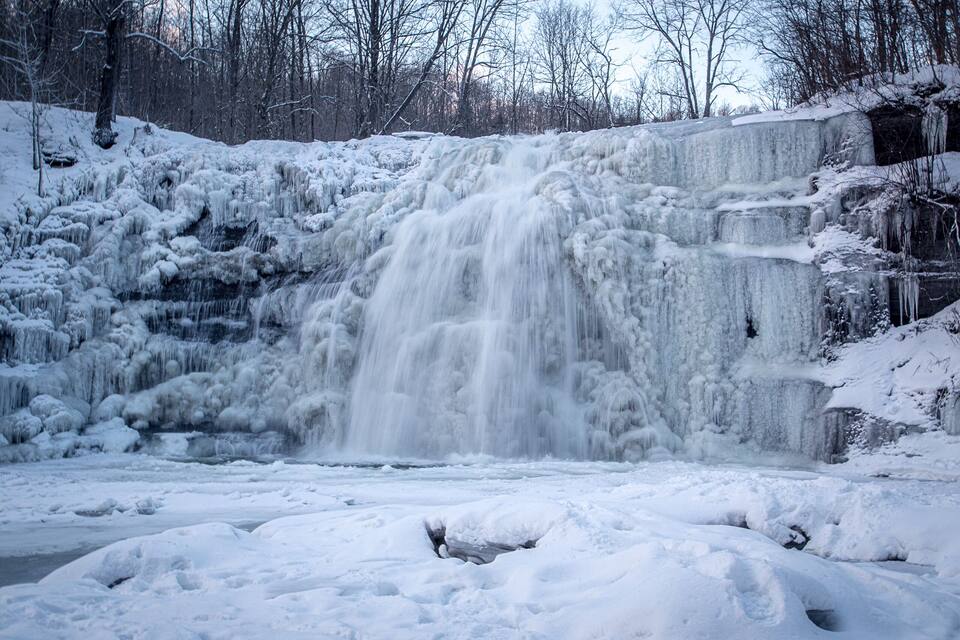 Une cascade gelée, entourée d’arbres couverts de neige.