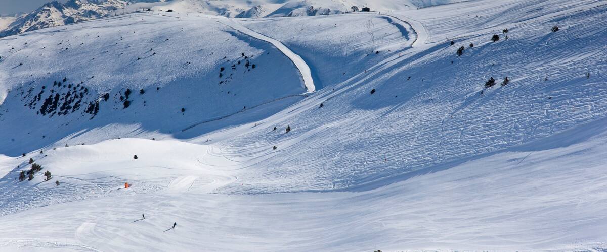 A snow-covered mountain landscape with ski tracks and a clear sky.