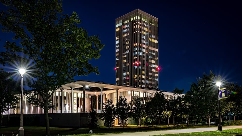 A modern building with illuminated windows at night, surrounded by trees and a well-lit pathway.