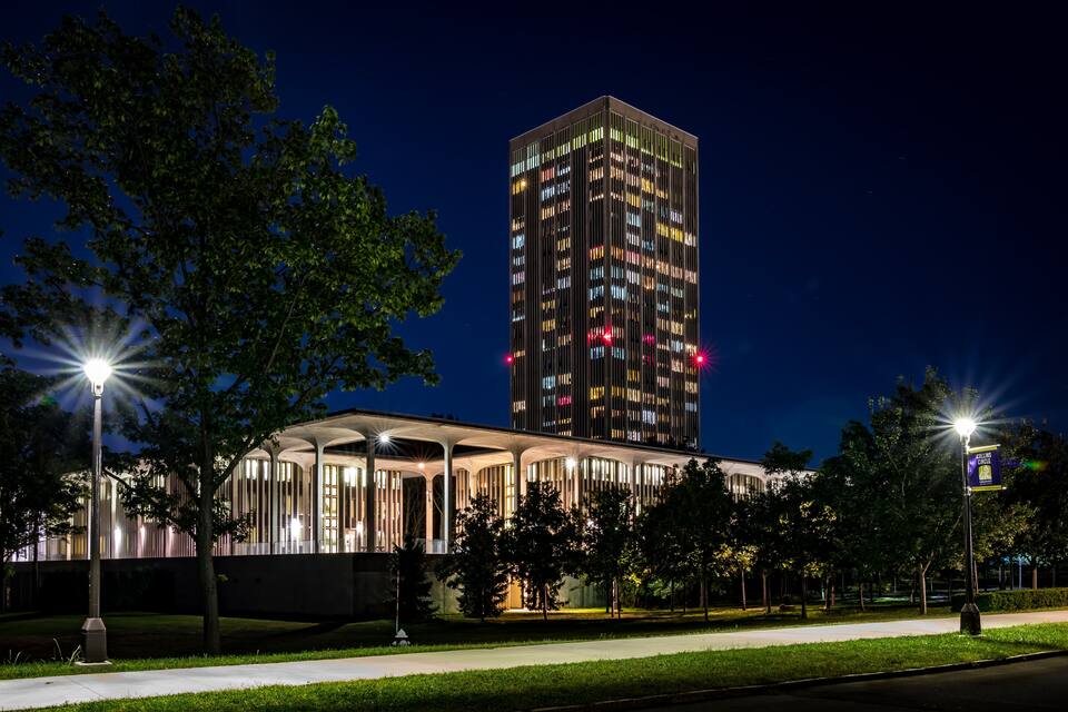Ein modernes Gebäude mit beleuchteten Fenstern bei Nacht, umgeben von Bäumen und einem gut ausgeleuchteten Weg.