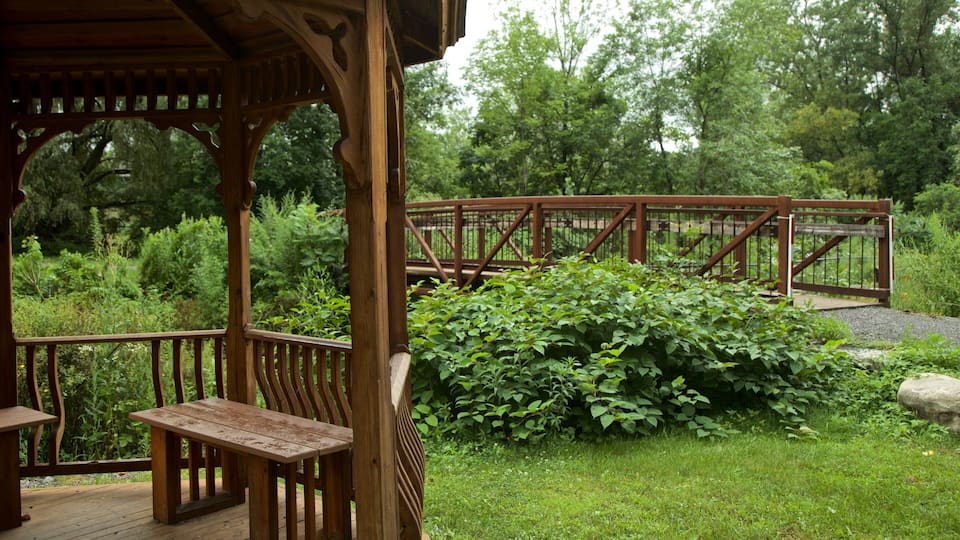 A wooden gazebo with benches, a wooden bridge, and lush greenery.