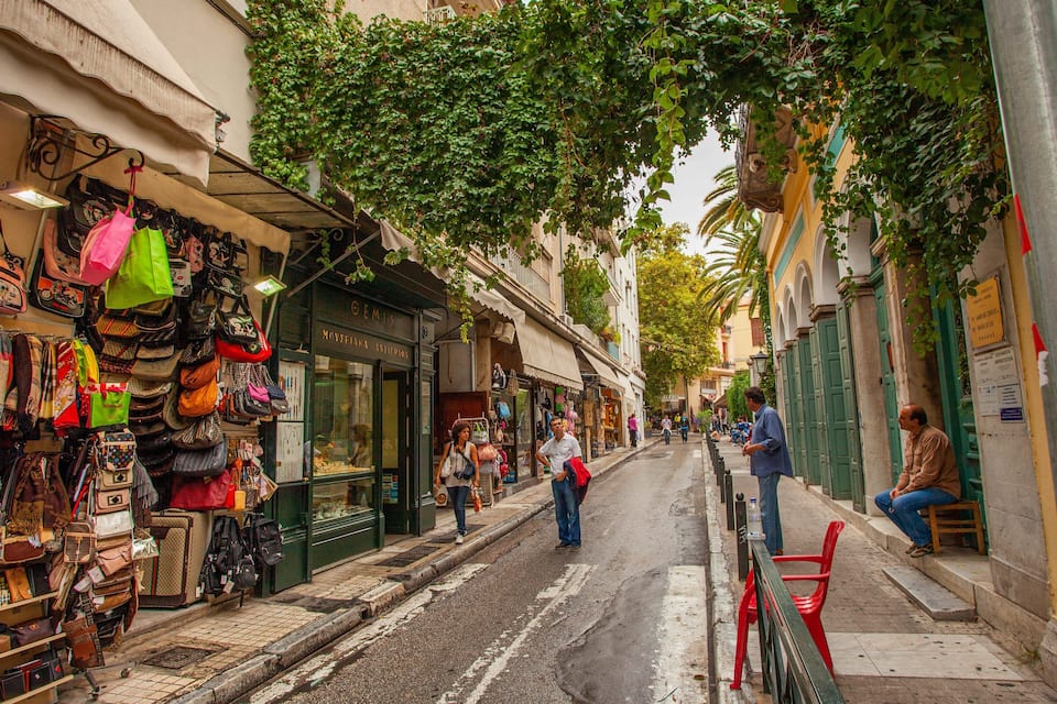 A narrow street with shops on both sides, including a store with bags and accessories.
