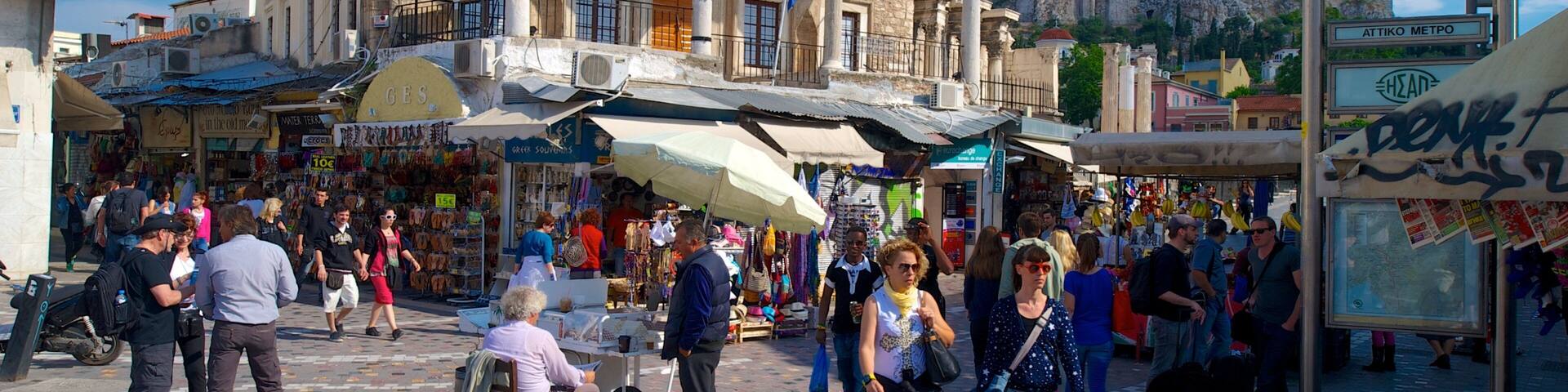 A bustling market street with historical architecture, including a building with arches and columns, and a prominent sign with a blue and white symbol.