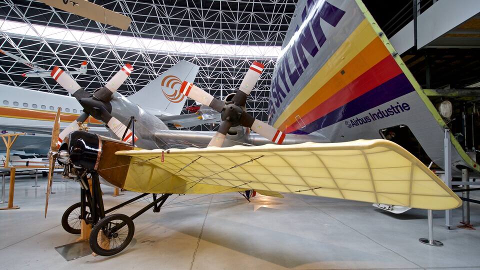 A vintage aircraft with a yellow wing and propellers, displayed indoors with a metal framework ceiling.