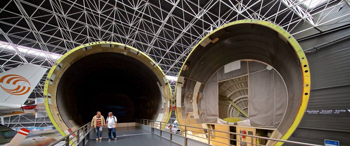 A large industrial building with two large cylindrical structures, a metal framework ceiling, and a walkway leading to an airplane.