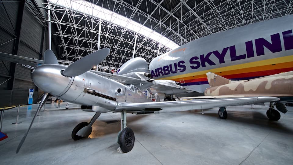 A vintage airplane with the text "AIRBUS SKYLINE" on its side, displayed in a museum with a high ceiling and metal framework.