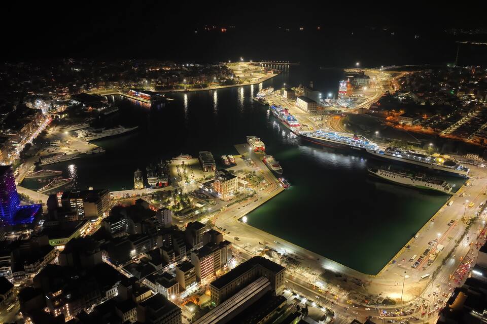 A nighttime aerial view of a city with a large body of water, illuminated buildings, and a bridge.