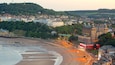 A coastal cityscape with a beach, historic buildings, and a green bridge.