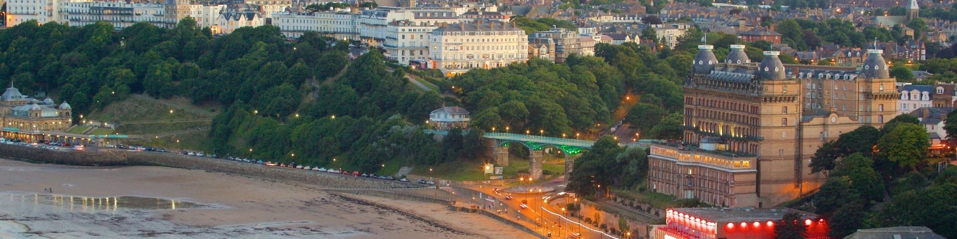 Paisagem costeira com uma praia, edifícios históricos e uma ponte verde.