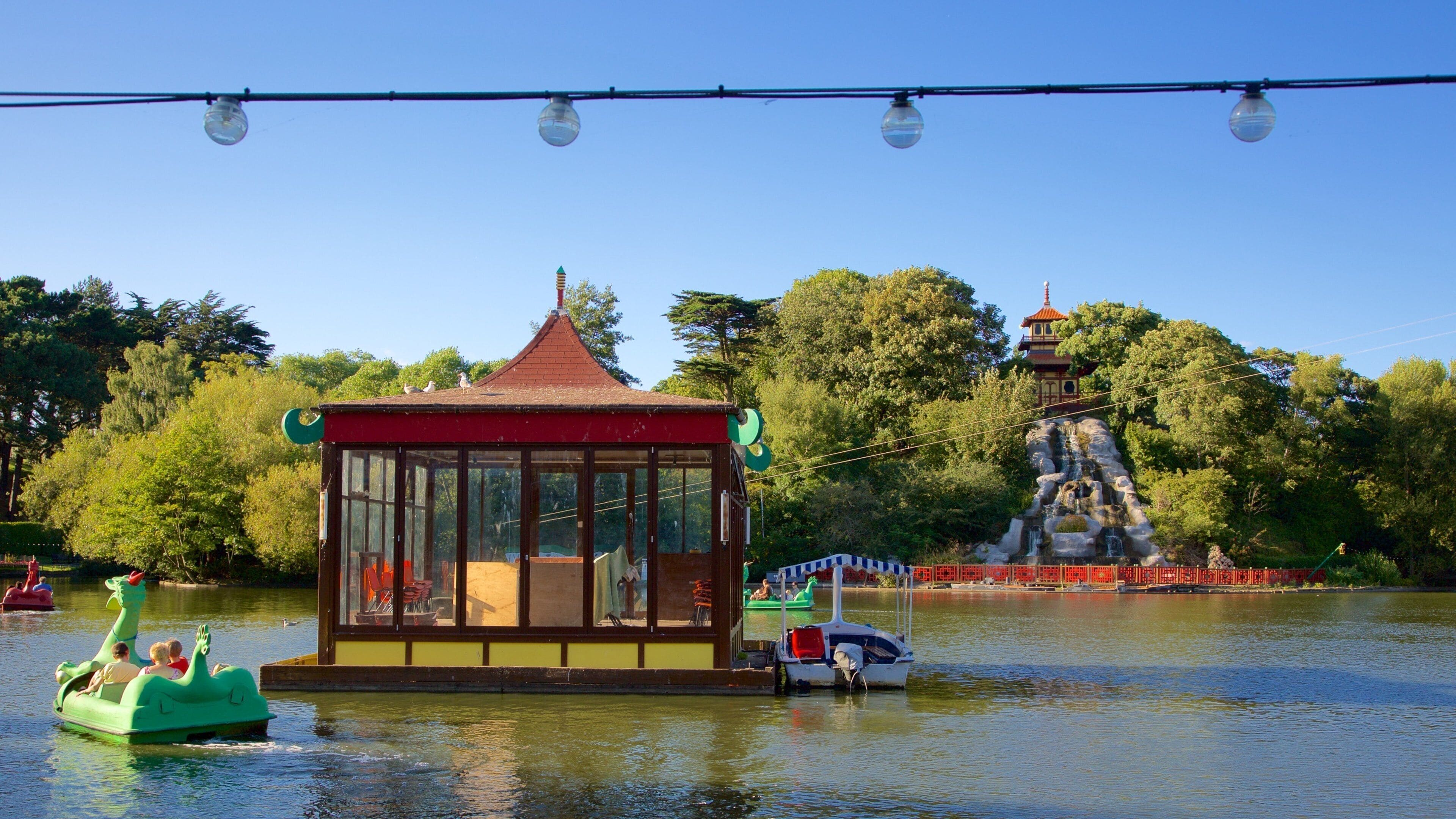 A glass-roofed pavilion by a lake, a green boat, and a pagoda-like structure in the background.
