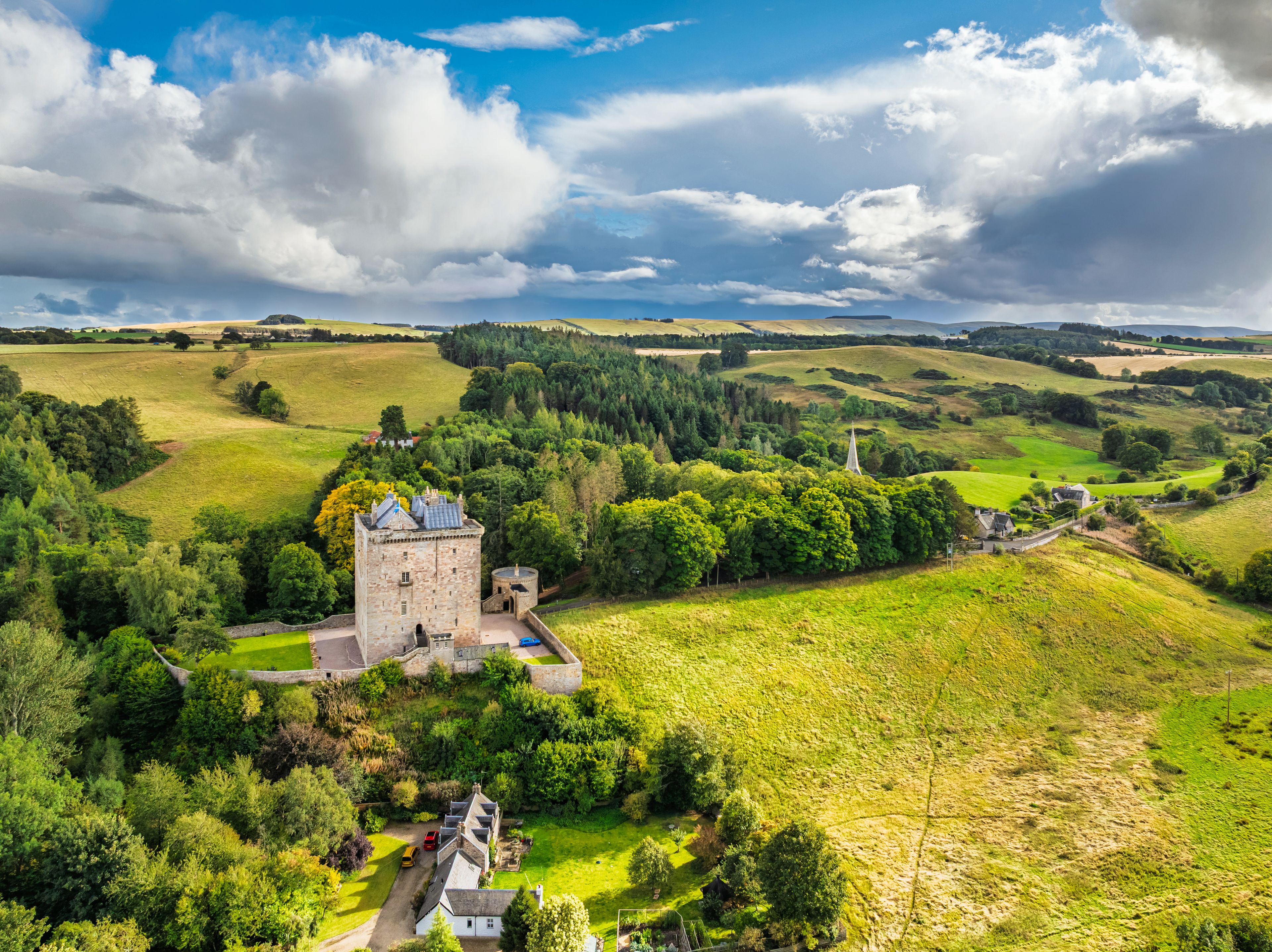 A castle surrounded by lush green fields and rolling hills under a partly cloudy sky.