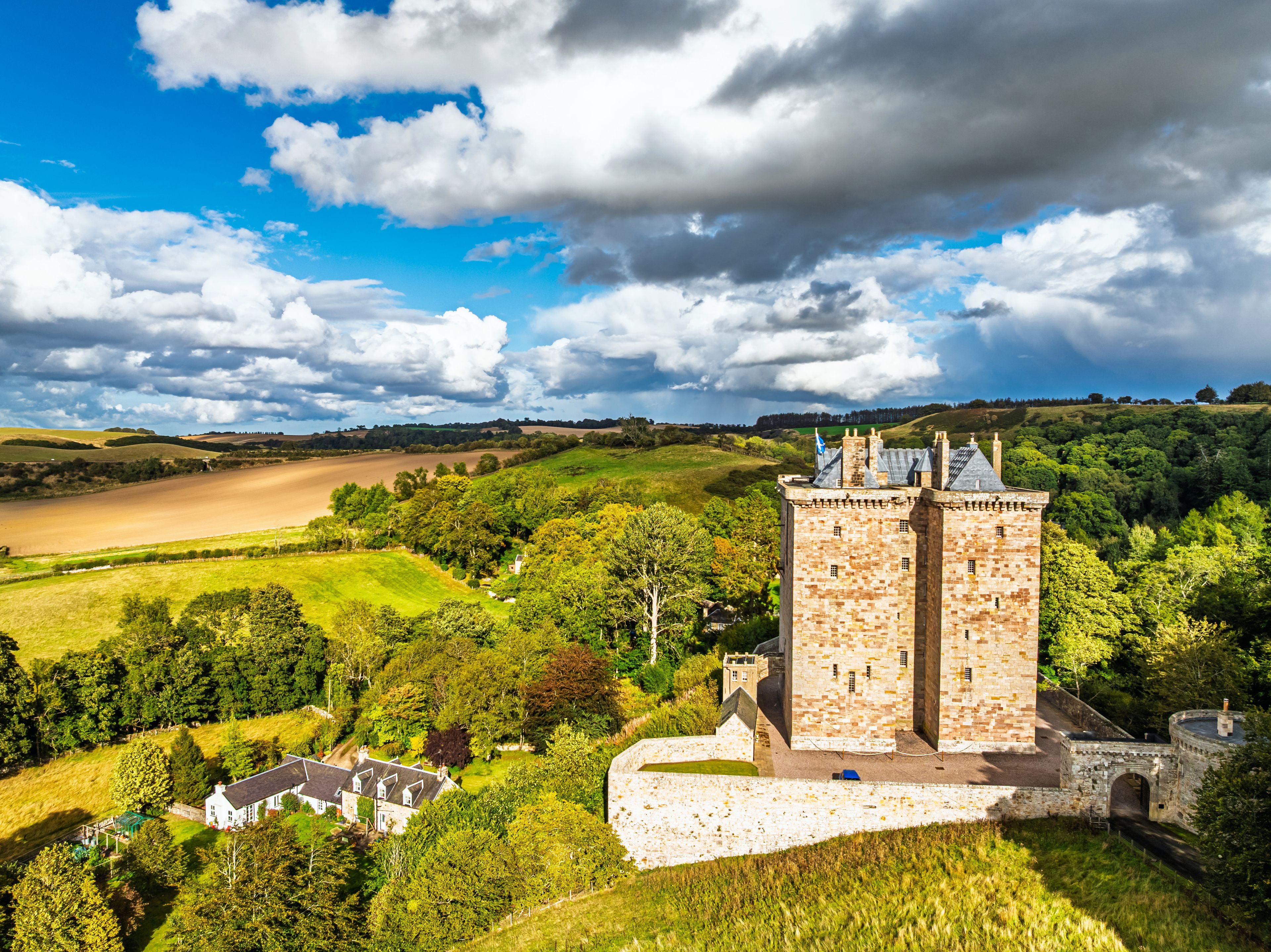 A castle surrounded by lush greenery and rolling hills under a partly cloudy sky.