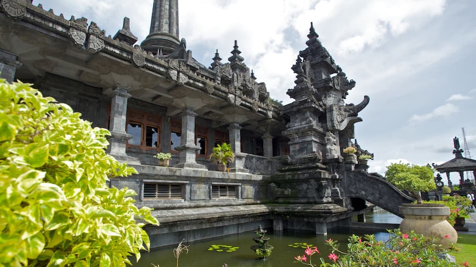 A traditional Balinese temple with intricate carvings, a central tower, and a surrounding pond with lotus flowers.