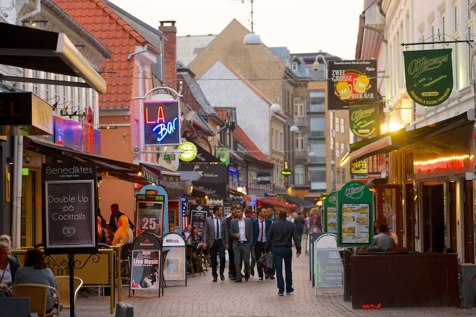 A bustling street with people walking, various shops, and signs for a bar and a restaurant.