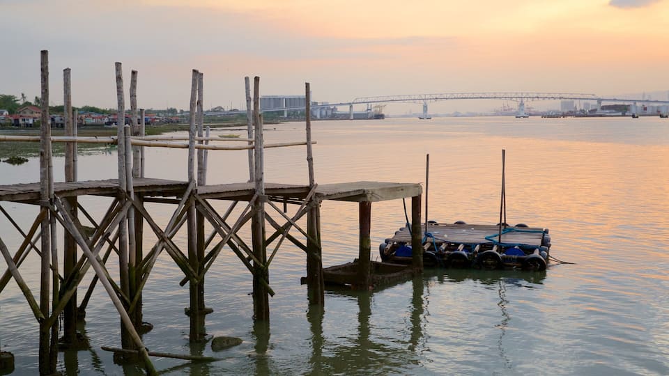 A wooden pier extending into calm water, a blue boat docked at the end, and a bridge in the background.