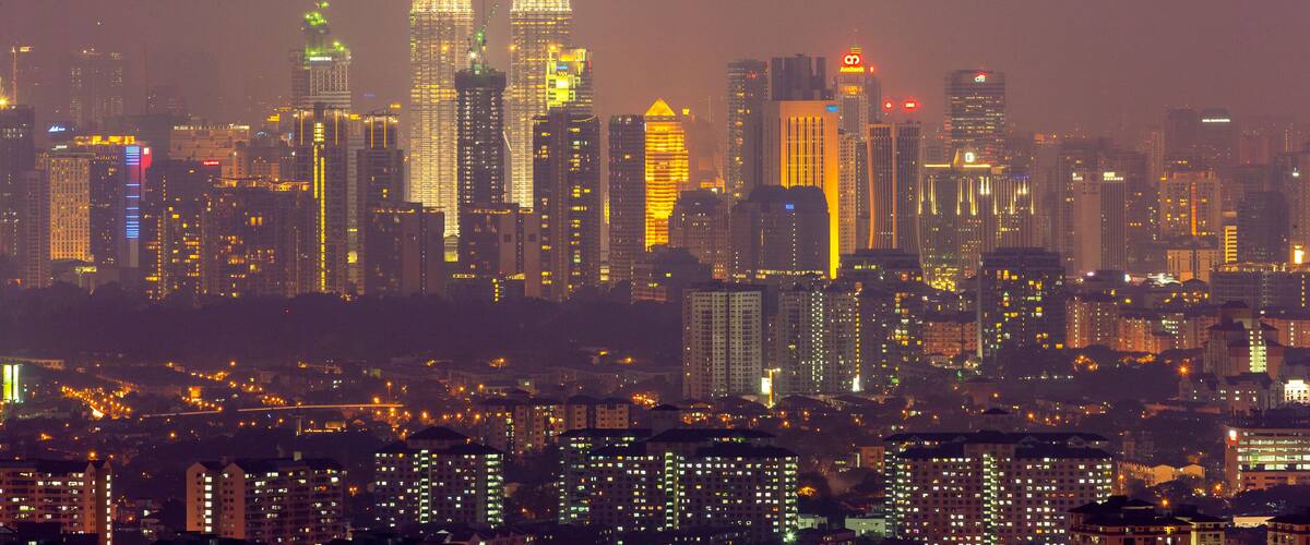 A cityscape at night with prominent twin skyscrapers, numerous other high-rise buildings, and a dense urban layout.