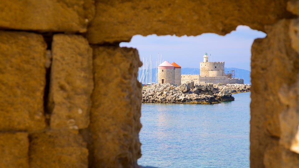 A stone wall with a view of a fortified island with a lighthouse and a tower.