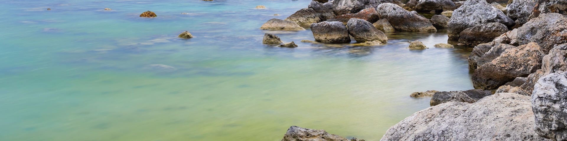 Mein Schiff 6 Cruise Ship docked beyond large ocean rocks in Montego Bay, Jamaica. Mountains in background landscape.