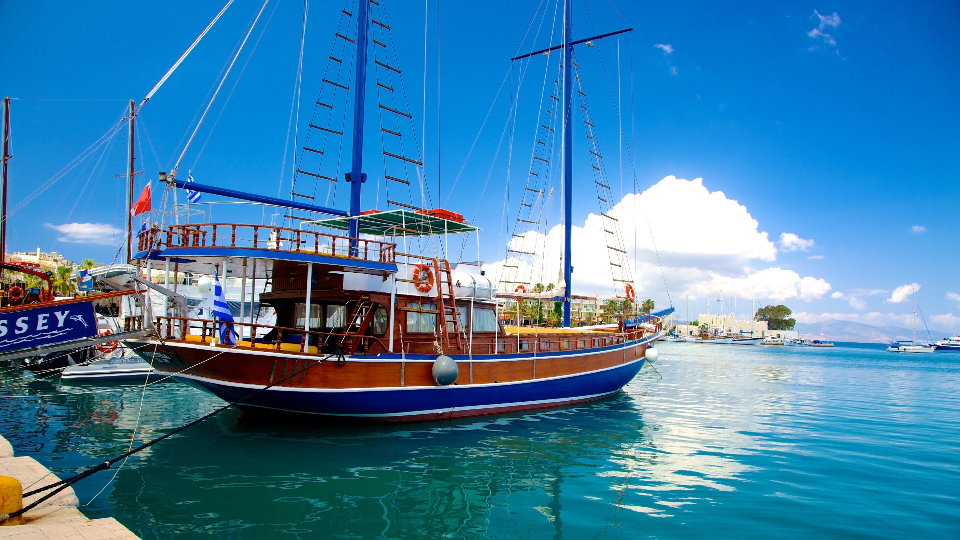 A traditional wooden boat docked at a marina with clear blue water and a sunny sky.