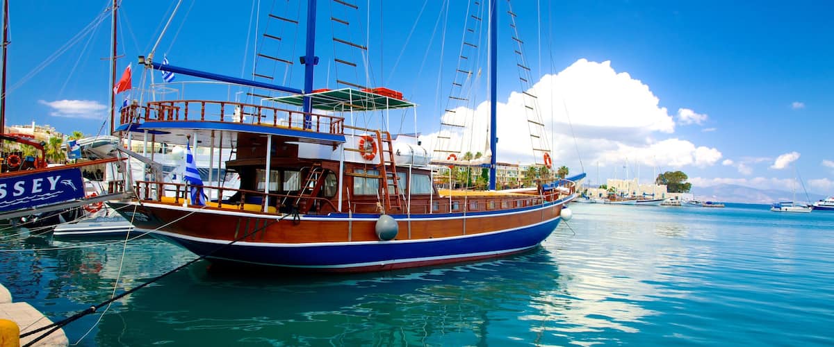 A traditional wooden boat docked at a marina with clear blue water and a sunny sky.