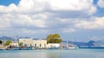 A harbor with several boats docked, a white building, and mountains in the background.