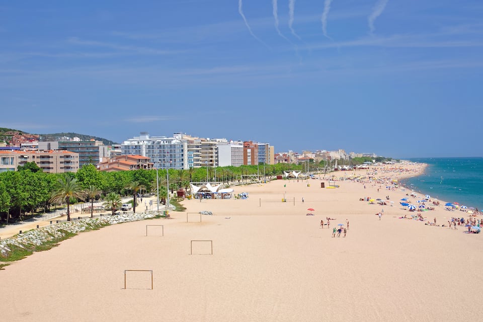 Ein Strand mit blauem Himmel, Palmen und Gebäuden im Hintergrund.