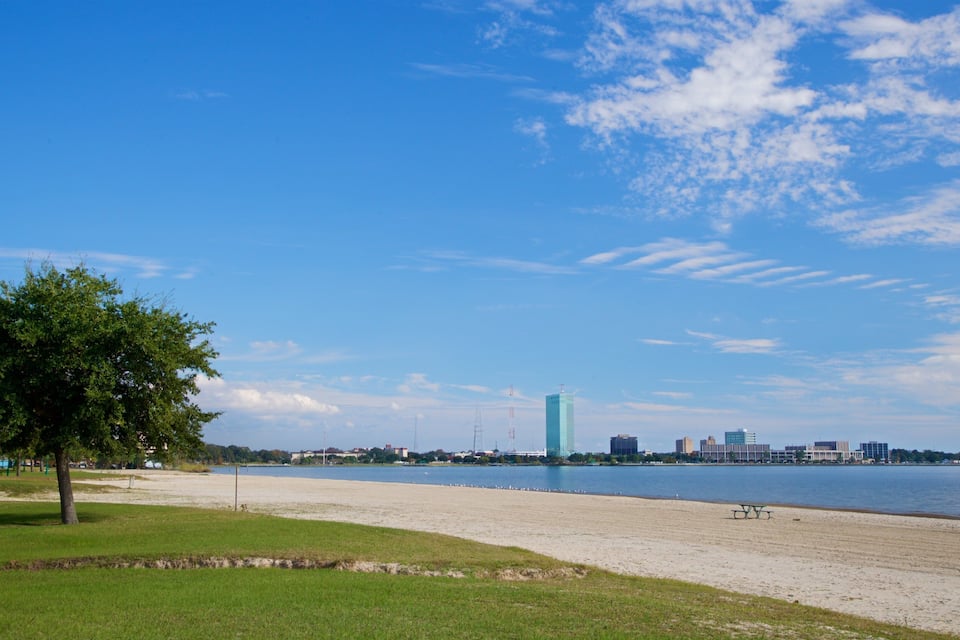 A lakeside park with a sandy beach, a picnic table, and a tall building in the distance.