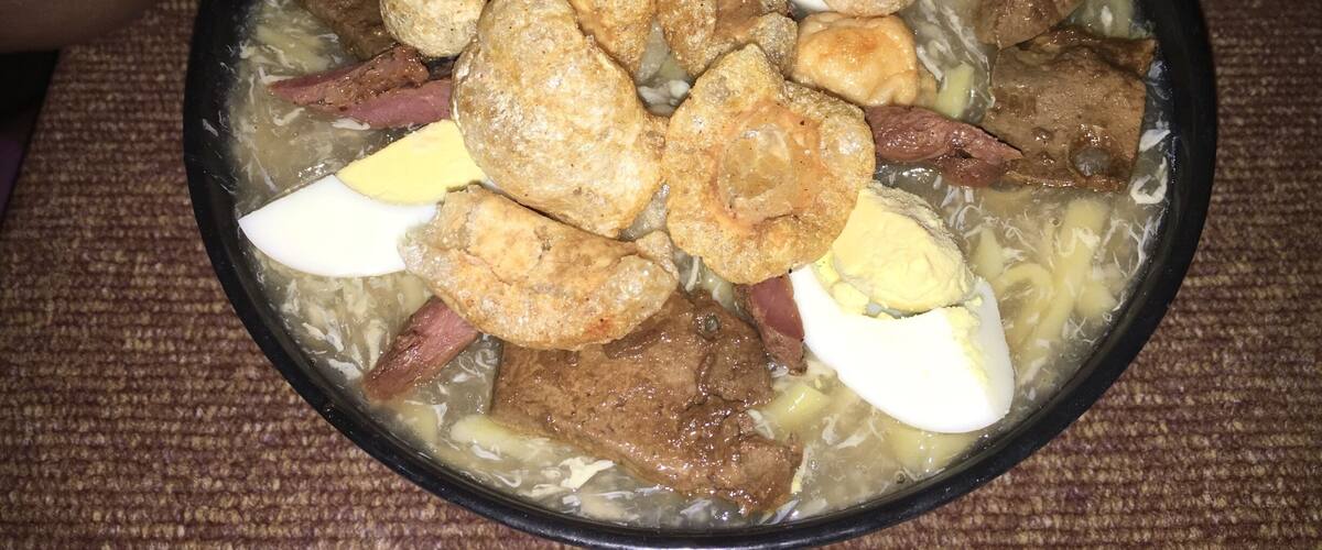 A bowl of soup with various ingredients like meat, eggs, and possibly tofu.