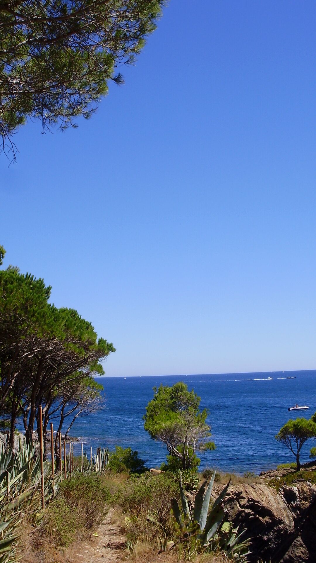 A coastal landscape with a clear blue sky, a rocky shoreline, and a body of water with boats.