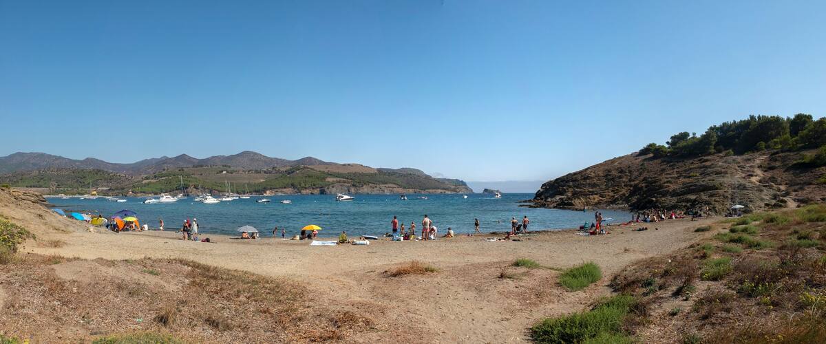 A beach with boats, people, and hills in the background.