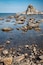 A rocky shoreline with clear water and a prominent rock formation in the distance.
