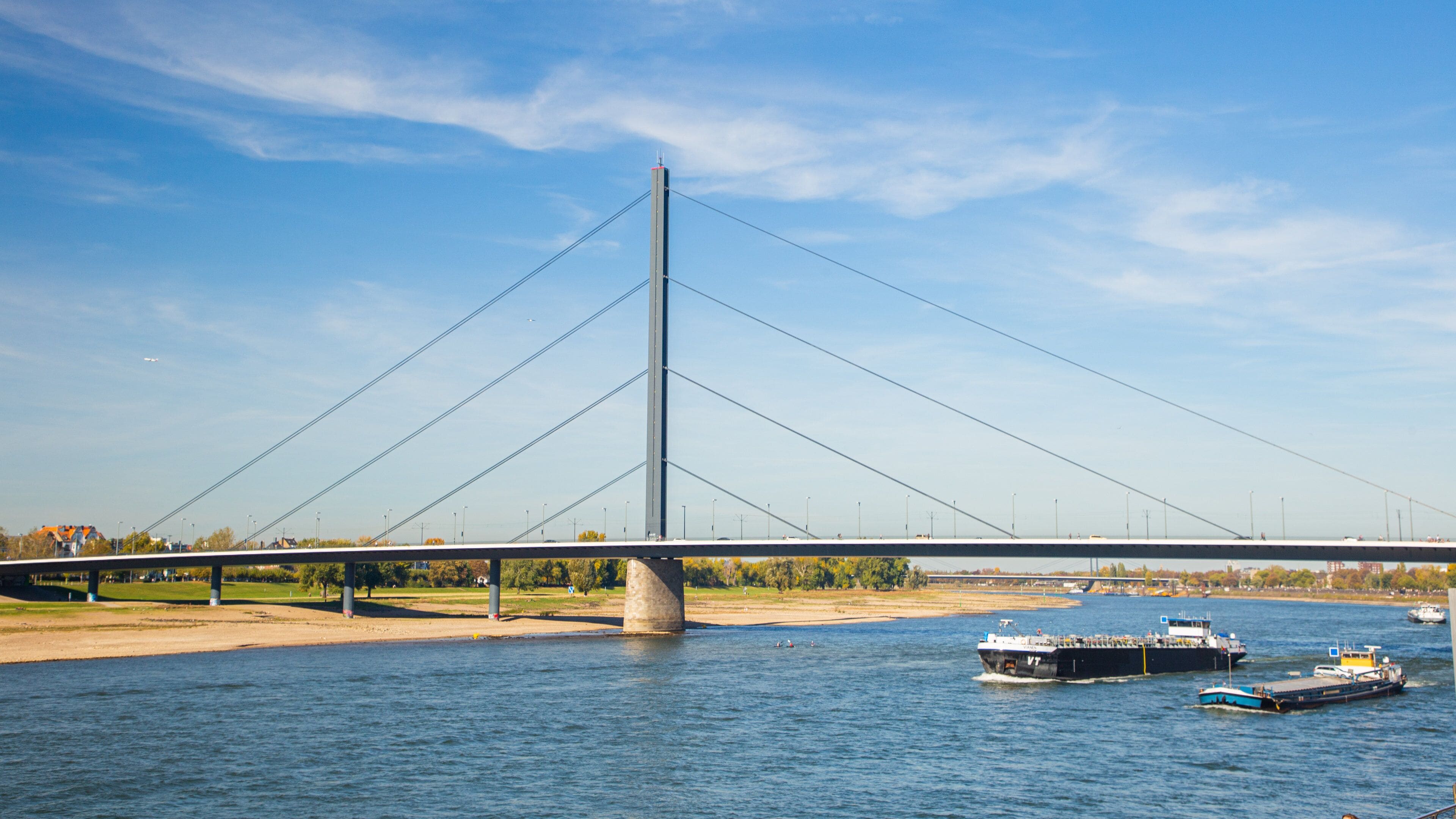 Eine Schrägseilbrücke über einem Fluss mit Booten und blauem Himmel.