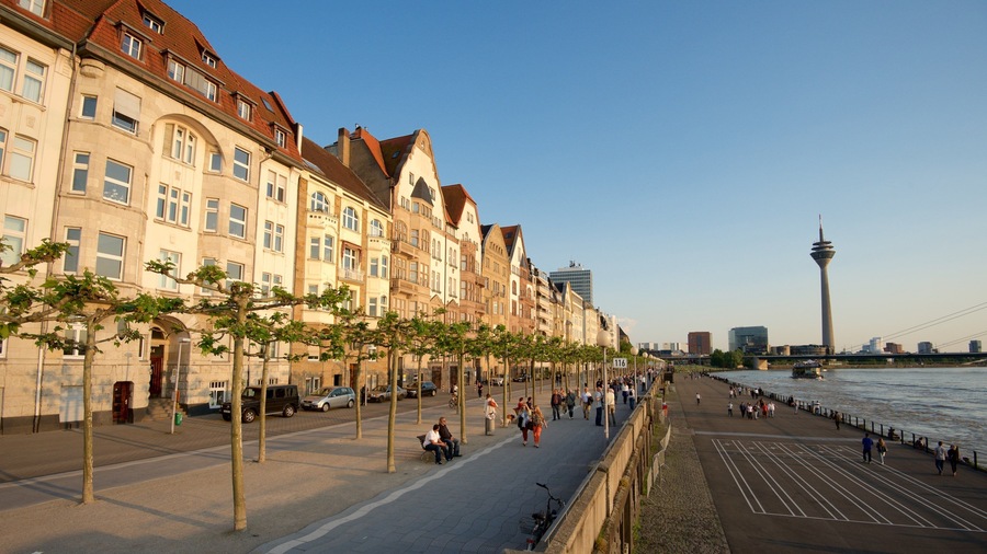 Een promenade aan de rivier met historische gebouwen, een moderne toren en een brug.