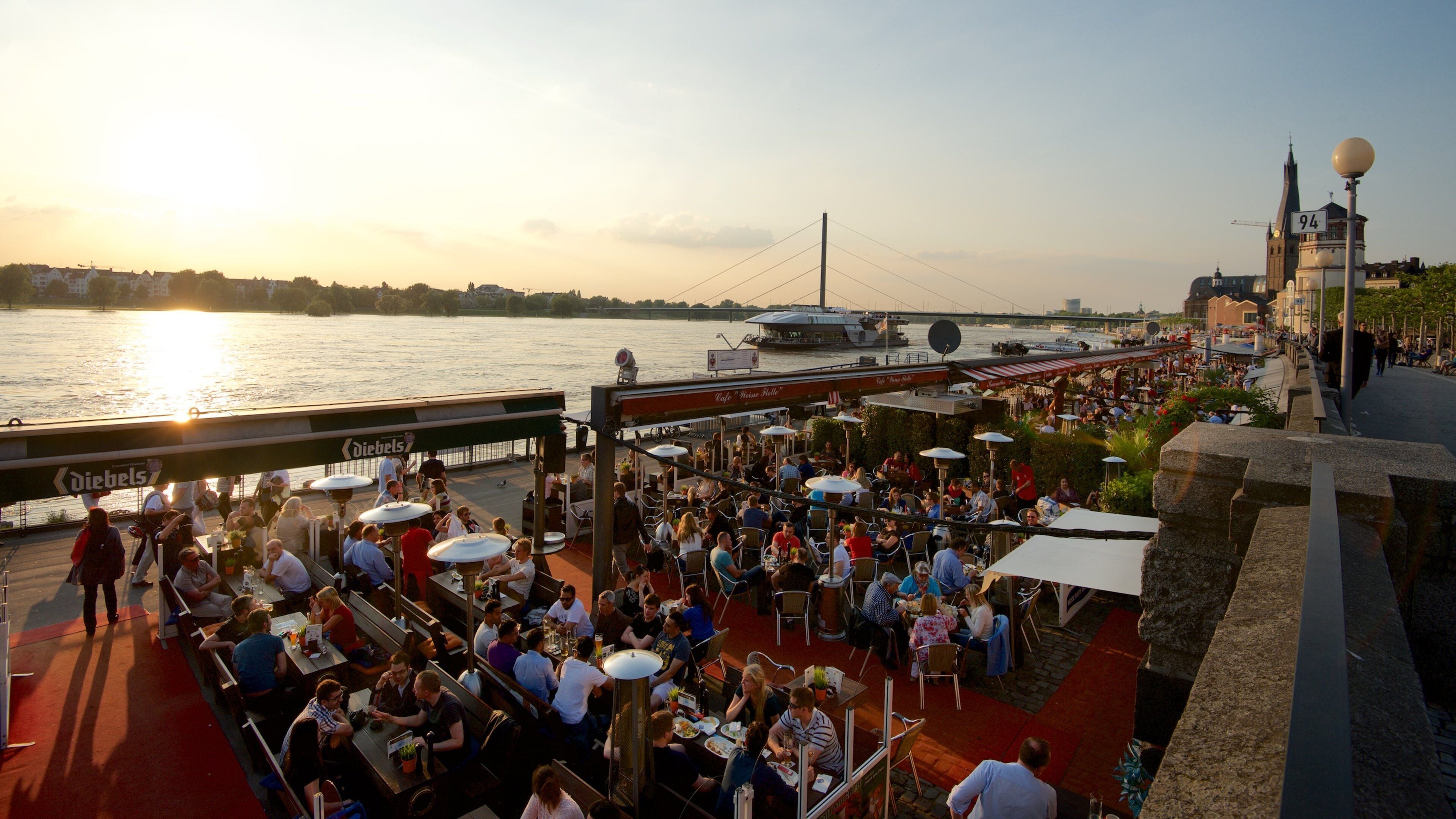Rheinuferpromenade mostrando comidas al aire libre, una bahía o un puerto y un atardecer