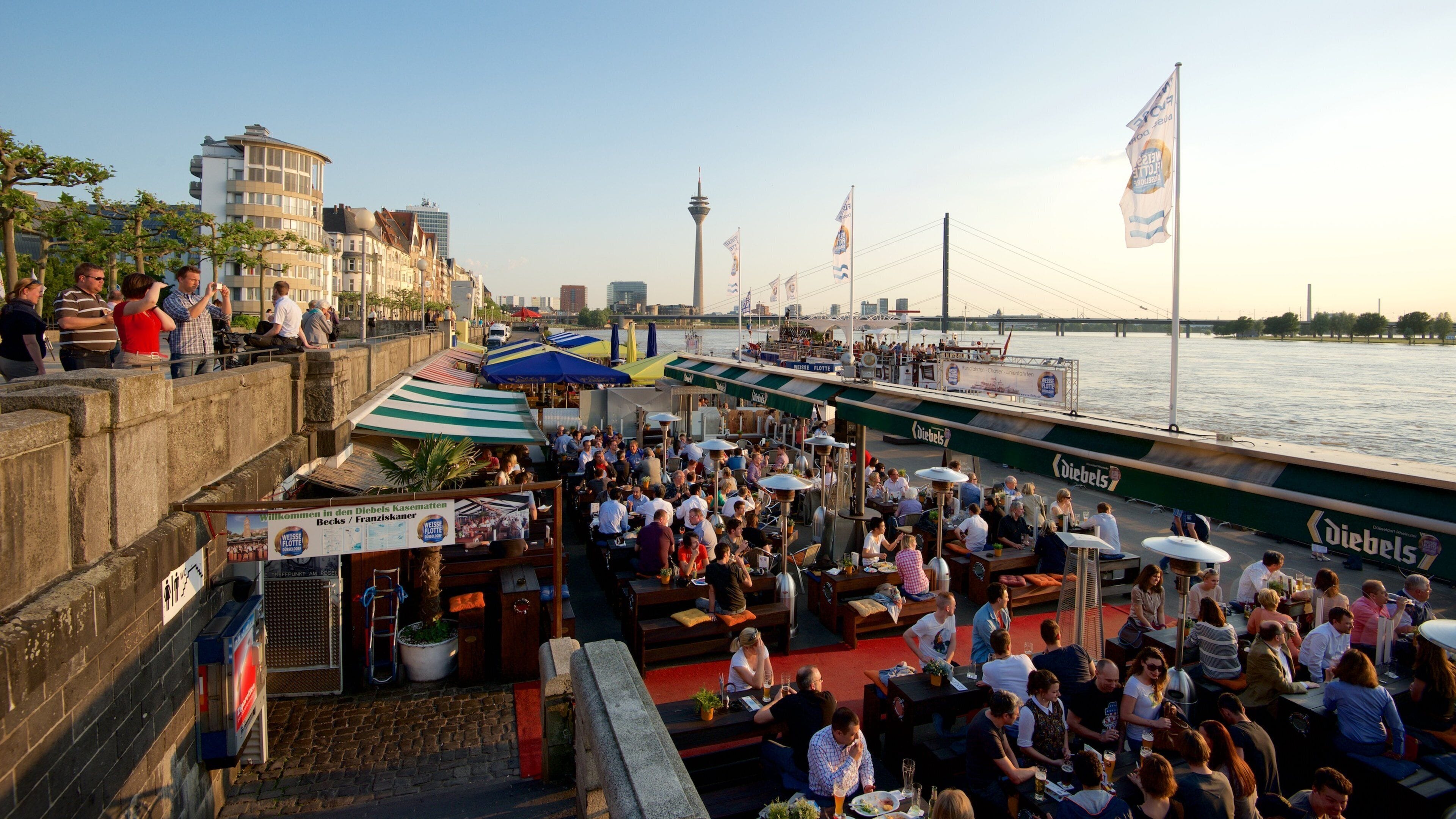 Rheinuferpromenade som viser udendørs spisning, en solnedgang og en bugt eller havn
