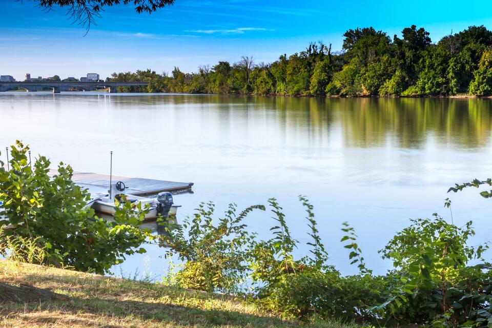 Un lac paisible, avec un quai, des arbres et un pont en arrière-plan.