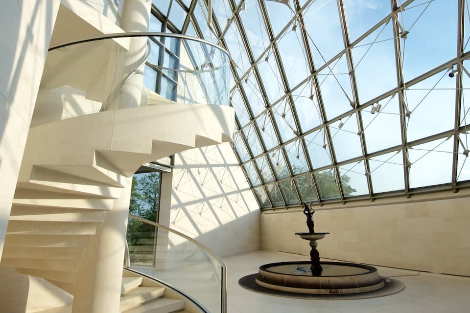 Een moderne spiraaltrap met glazen balustrades en een fontein in het midden.